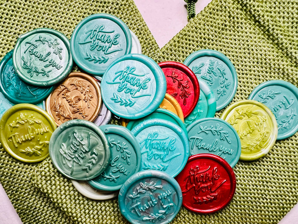 Holiday 'Thank You' wax seal stickers created by Rochambeau Home in various colors and showcased on green burlap bags.