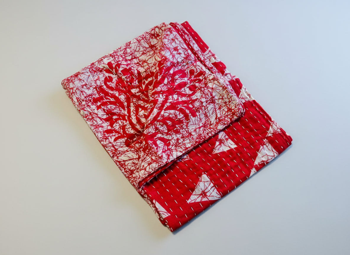 A vibrant red, white, and geometric patterned Kantha kitchen towel on a gray background. 