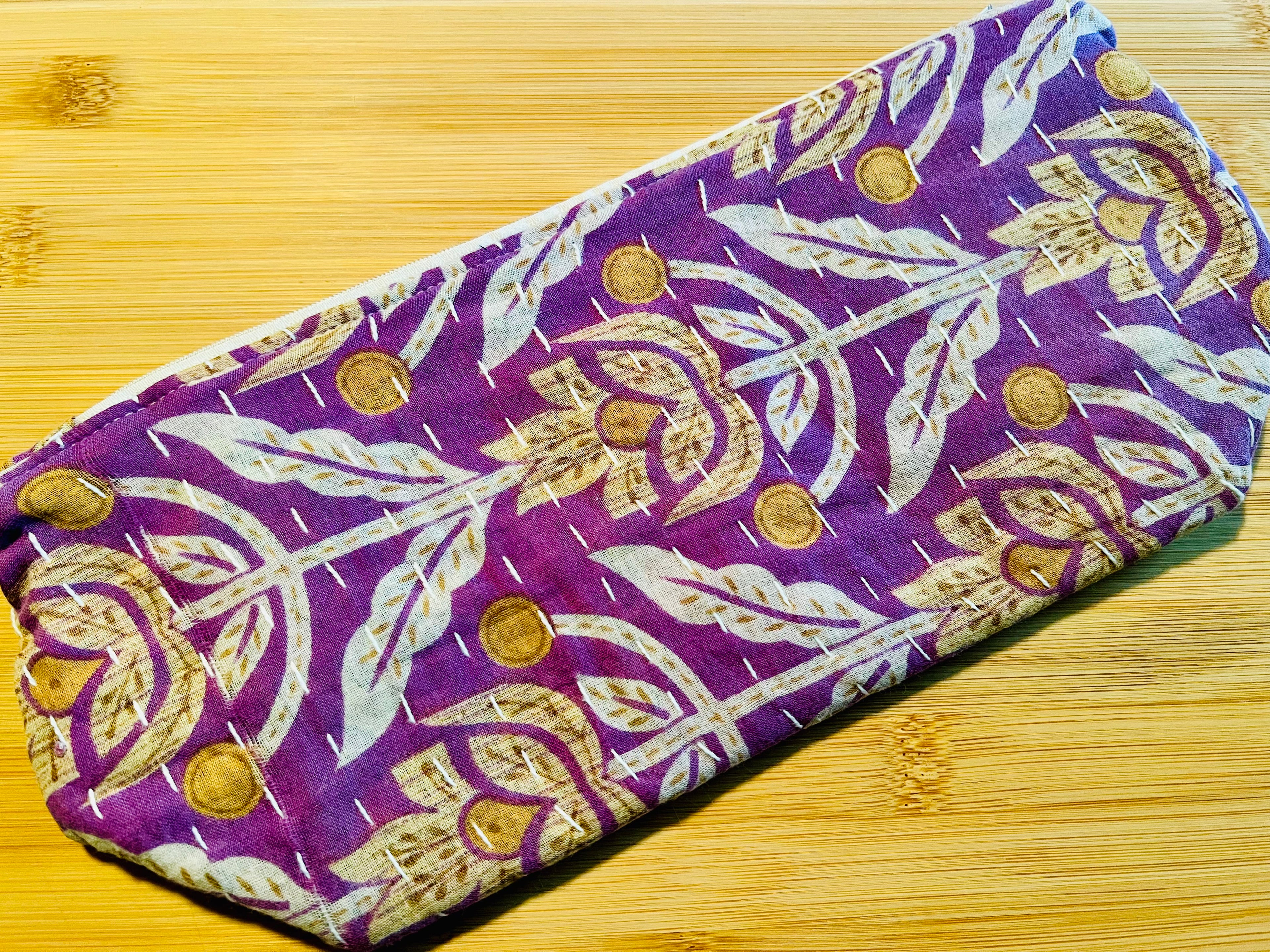 Purple fabric pouch with gold floral patterns on a wooden surface