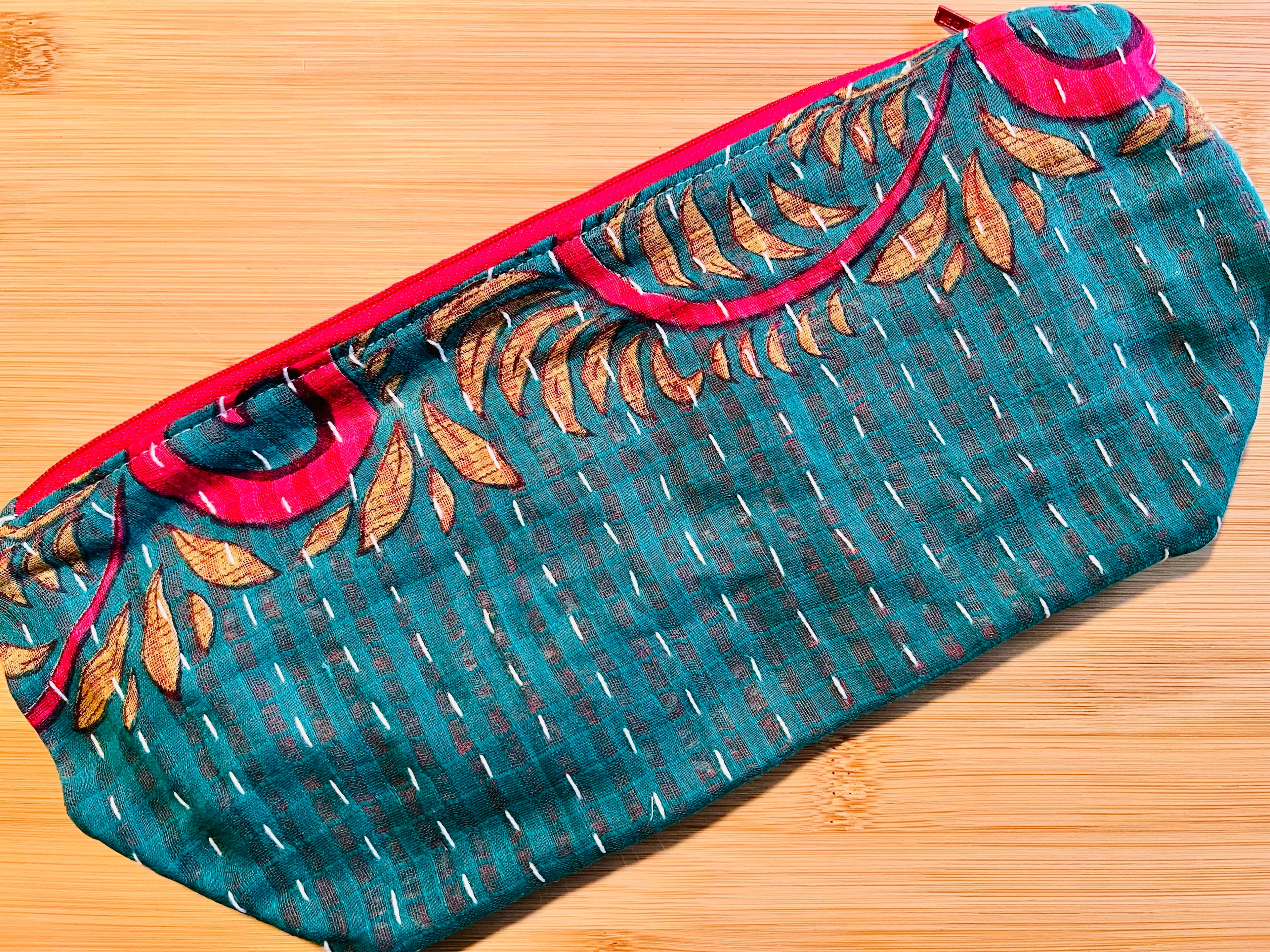 Teal clutch bag with gold leaf pattern and red accents on a wooden surface