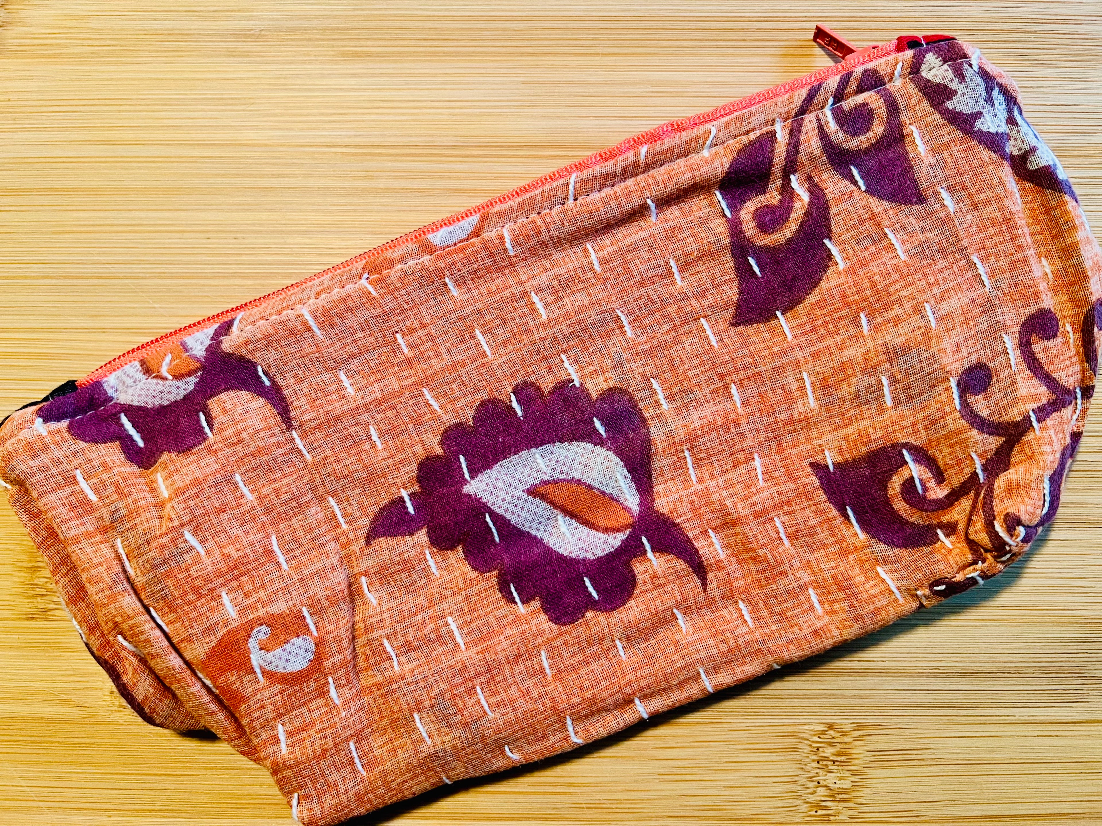 Fabric pouch with purple and white patterns on an orange background, placed on a wooden surface.