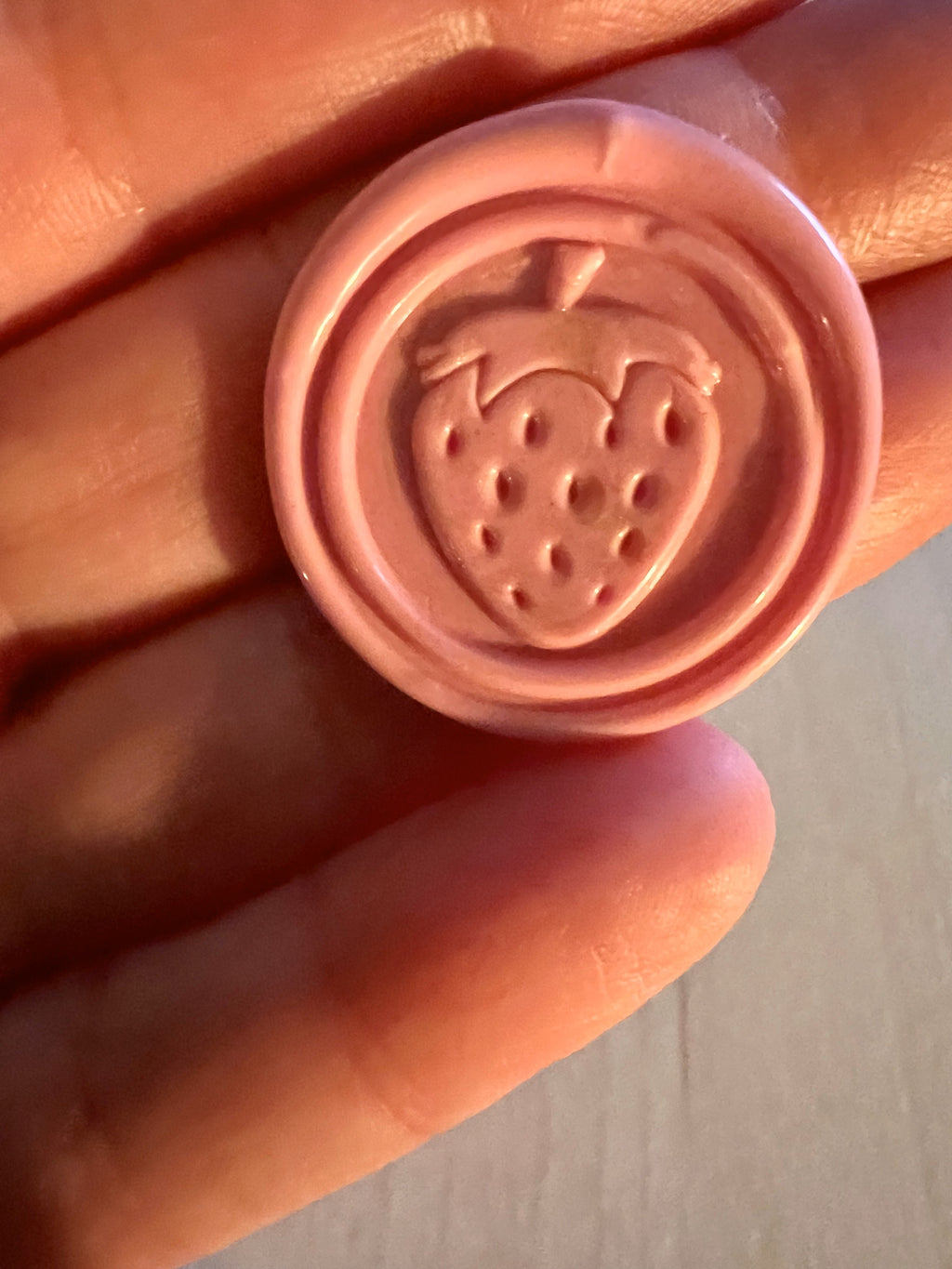 Close up view of a cute strawberry wax seal sticker in a pink color