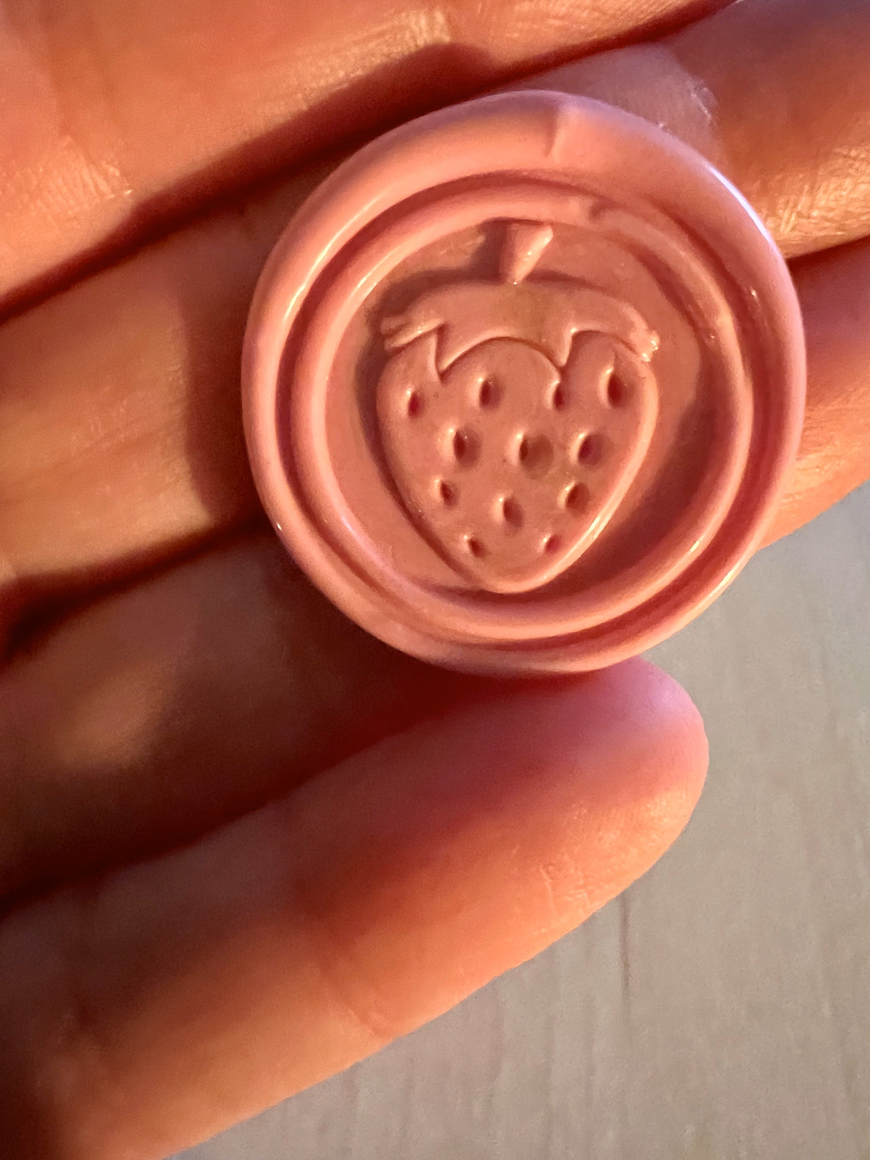 Close up view of a cute strawberry wax seal sticker in a pink color
