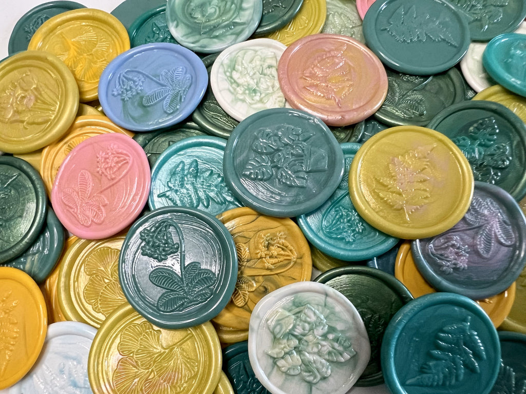 Garden-inspired wax seal stickers in shades of green, yellow, pink, and blue arranged on white stationery