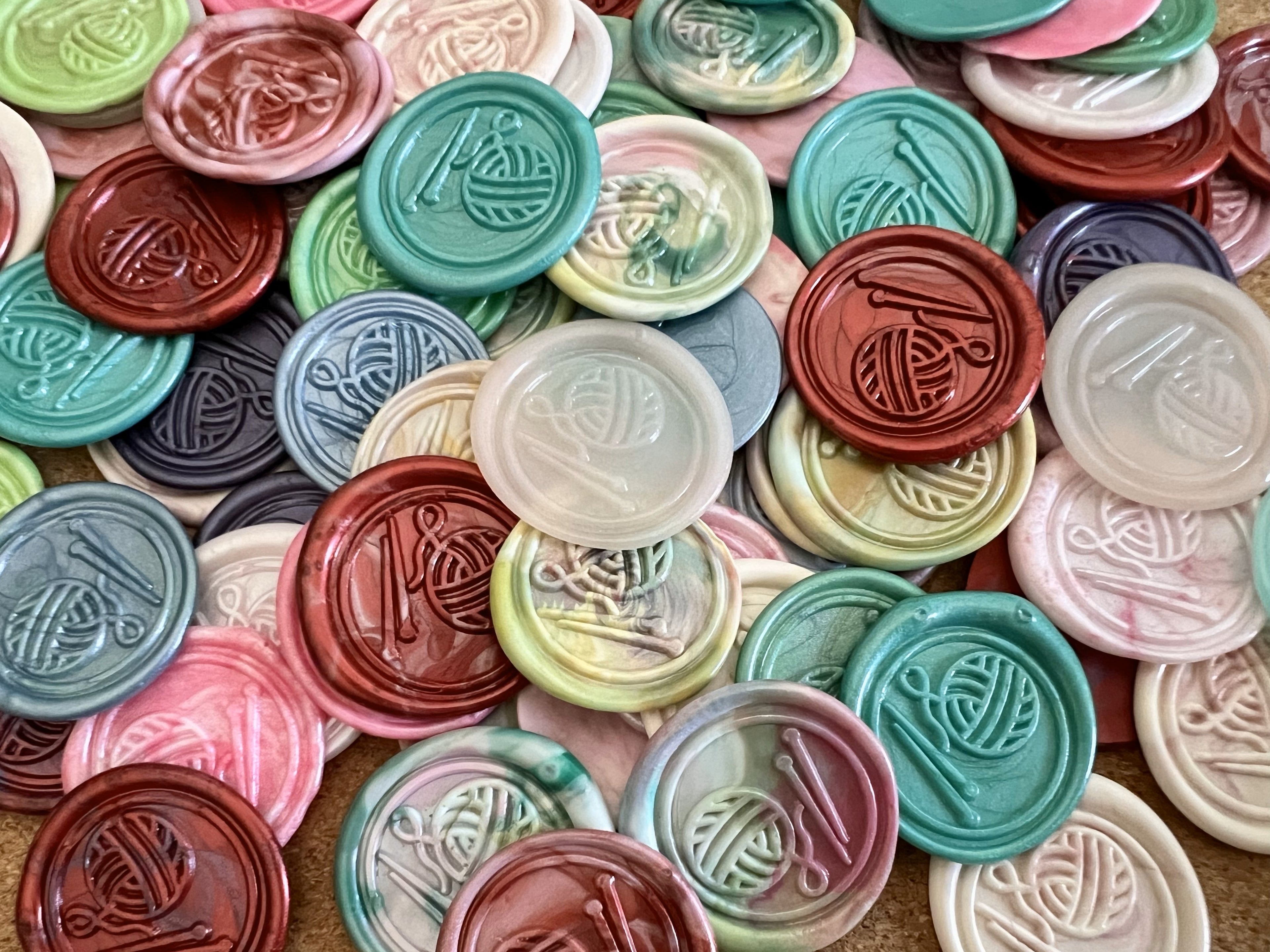 Close-up of wax seal sticker featuring a ball of yarn and knitting needles 