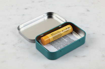 Small metal tin with a yellow chapstick and medication wrapper inside on a white background