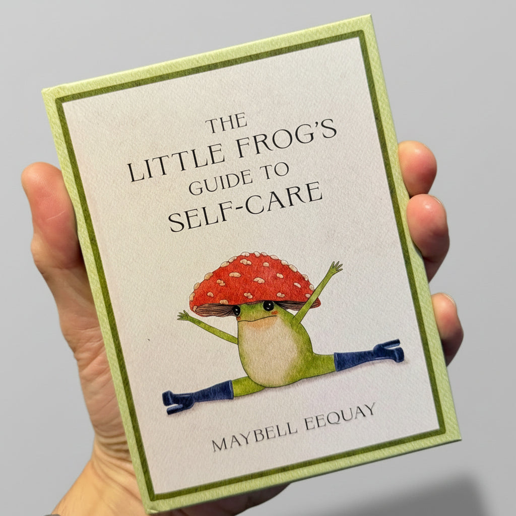 Book titled 'The Little Frog's Guide to Self-Care' held by a hand with a brown background