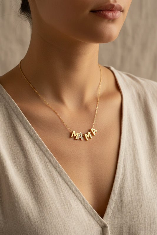 Gold necklace with 'MAMA' pendant from Rochambeau Home on a neutral background and with a beige top