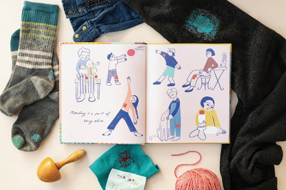 Open book with illustrated pages surrounded by yarn and fabric on a white surface