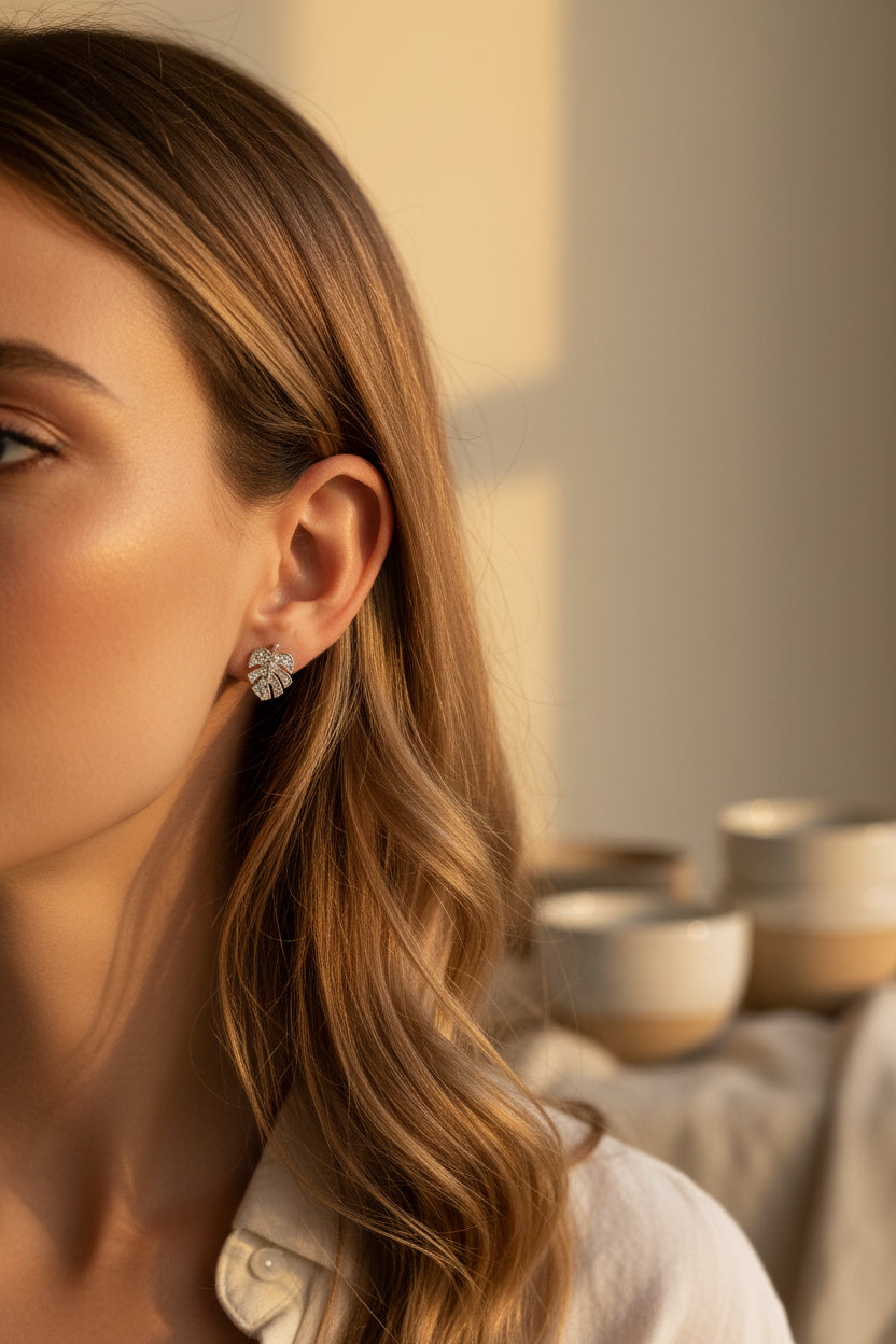 Monstera leaf earrings being worn with a background of blurred images and a neutral background