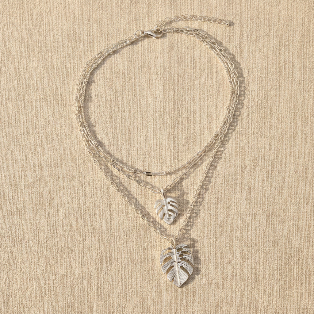 Silver leaf necklaces on a beige surface with a neutral background