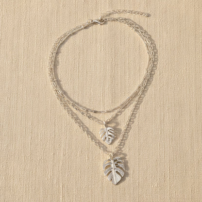 Silver leaf necklaces on a beige surface with a neutral background