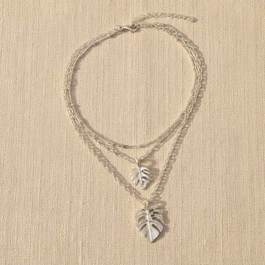 Silver leaf necklaces on a beige surface with a neutral background