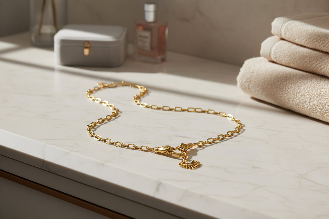 Gold chain necklace on a marble surface with towels and a bottle in the background