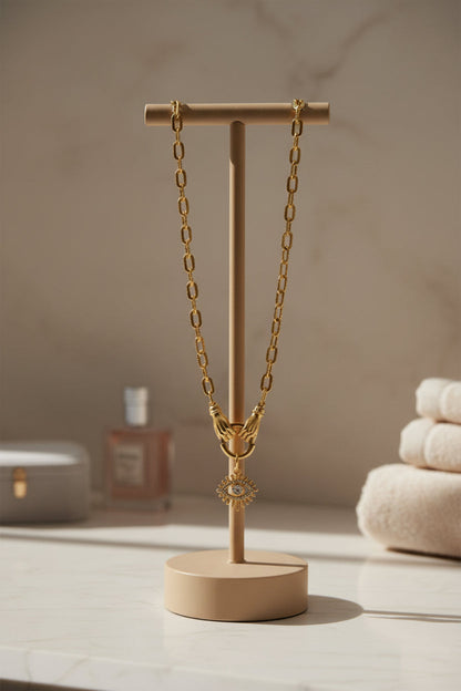 Gold chain necklace with hands holding an evil eye pendant with a bathroom decor background and neutral colors