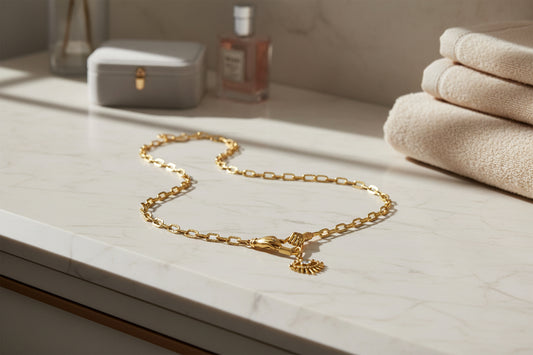 Gold chain necklace on a marble surface with towels and a bottle in the background
