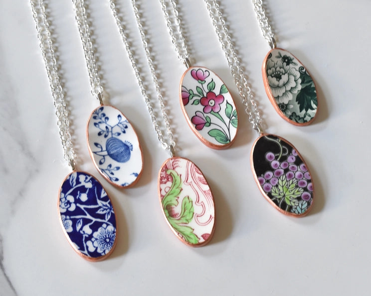 Close-up of six unique broken china necklaces, each featuring a distinct porcelain shard and silver-plated chain.