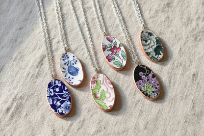 A collection of three oval-shaped necklaces made from recycled china, each featuring a different floral pattern with rose gold trim on a silver chain.