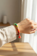 Hand wearing a colorful rainbow beaded bracelet with a tassel on a neutral background from Rochambeau Home Gifts