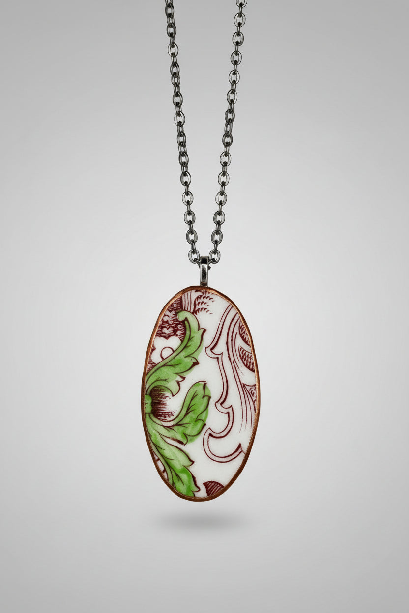 Oval-shaped pendant with red and green leaf design on a white background