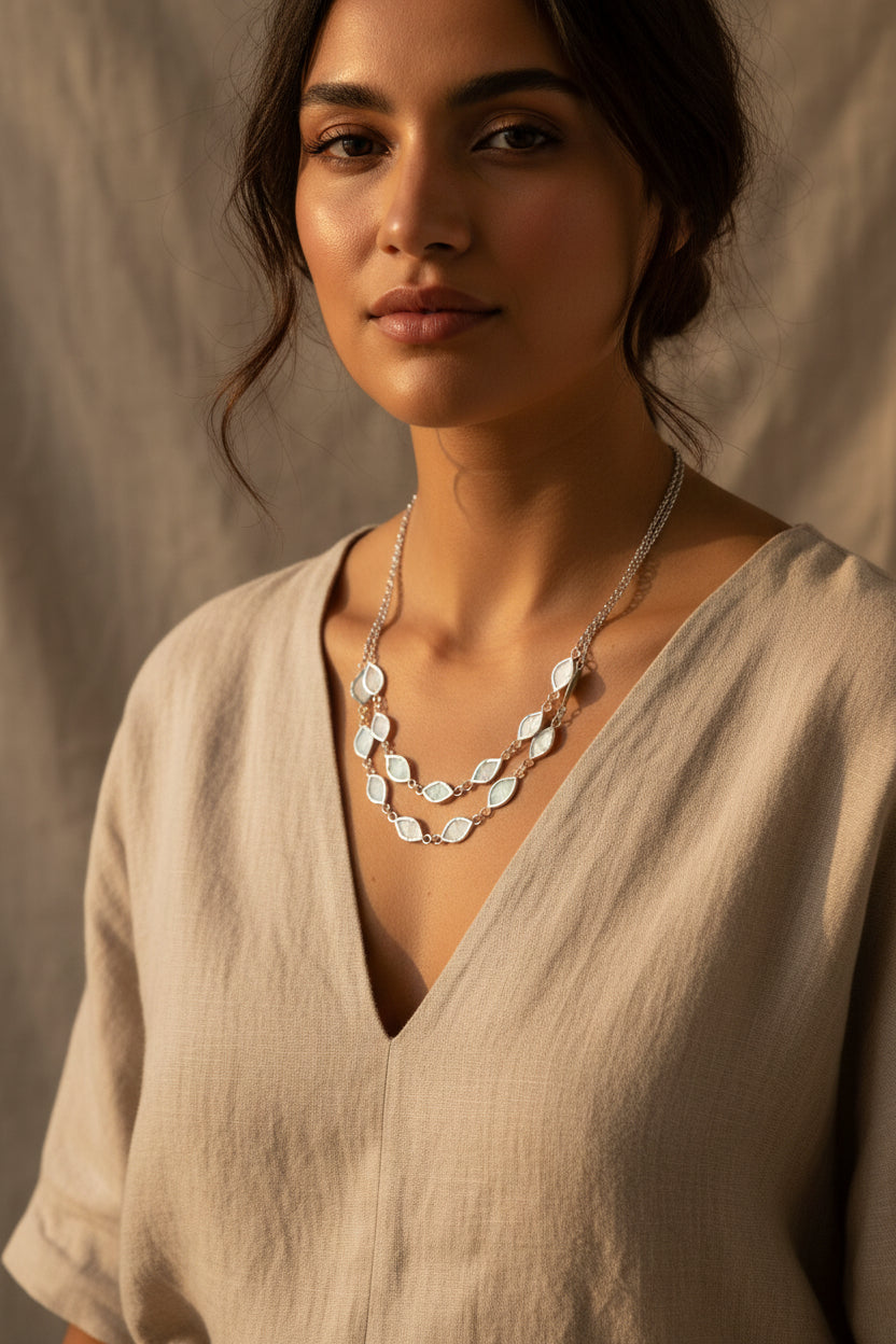 Silver necklace with leaf-shaped pendants being worn by a with a beige garment against a neutral background