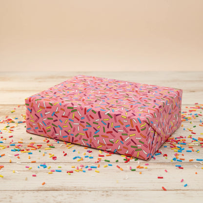 Pink gift box with colorful sprinkles pattern on a beige background