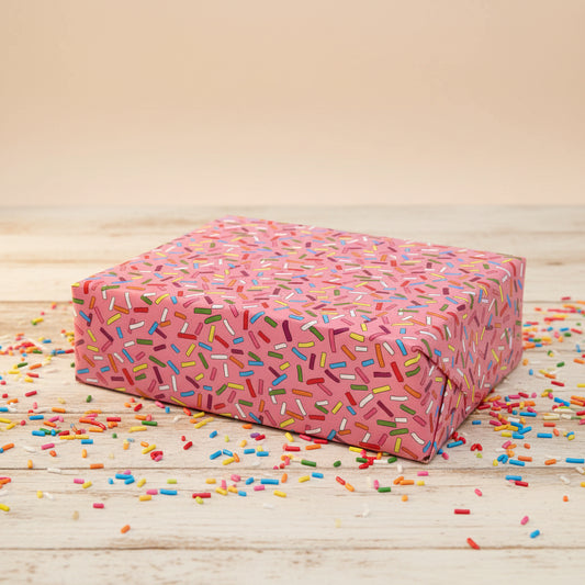 Pink gift box with colorful sprinkles pattern on a beige background