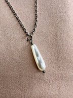 Close of view of Mother of Pearl drop necklace on a backdrop pf pink suede showcasing the iridescent pearl