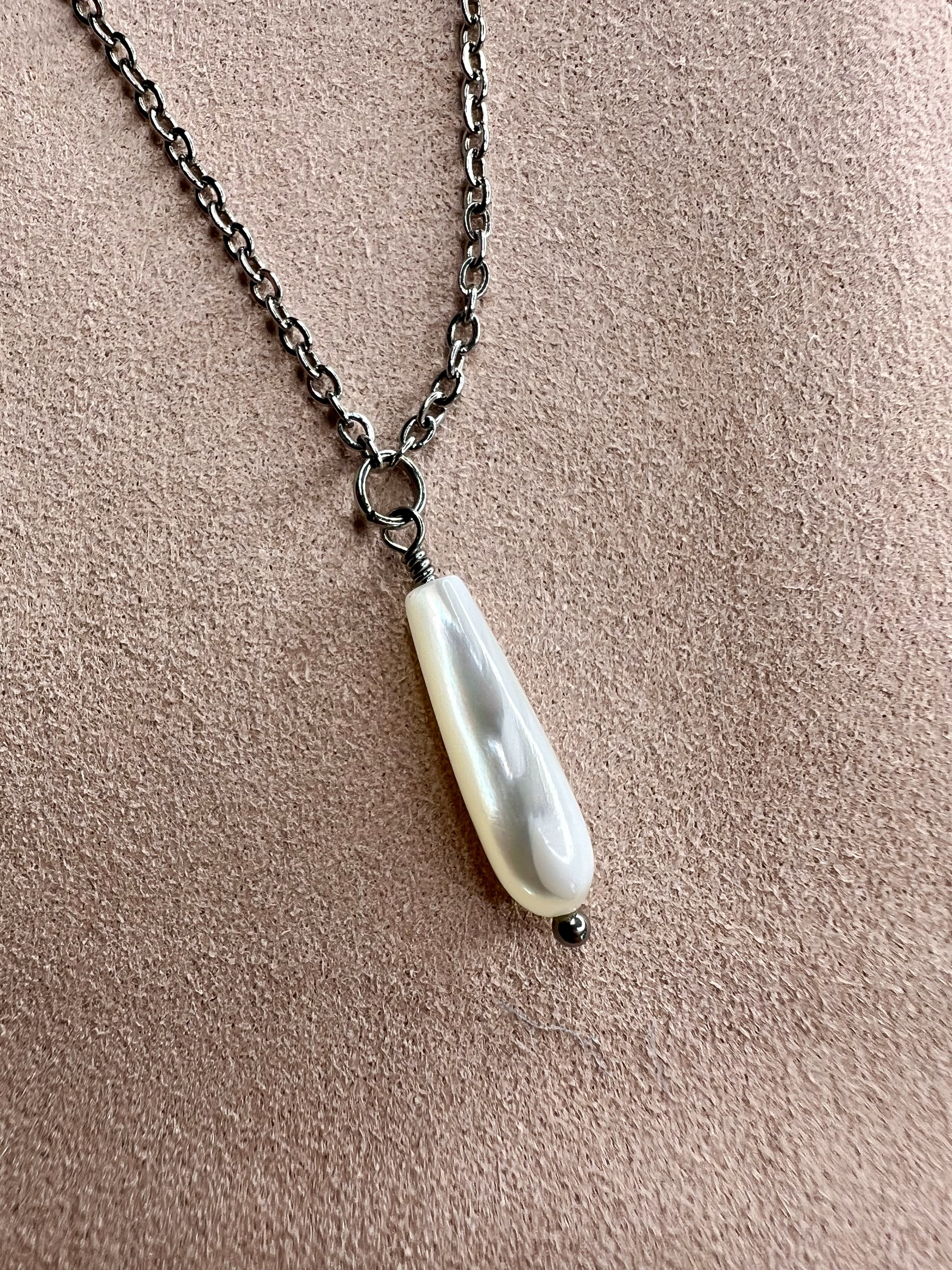 Close of view of Mother of Pearl drop necklace on a backdrop pf pink suede showcasing the iridescent pearl