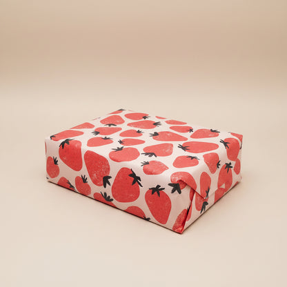 Bright and fun strawberry gift wrap around a present on a light gray background