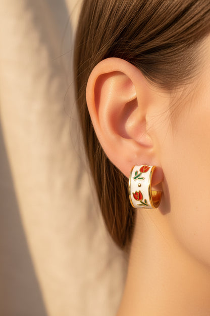 Gold and white earrings with floral design being worn against a beige background