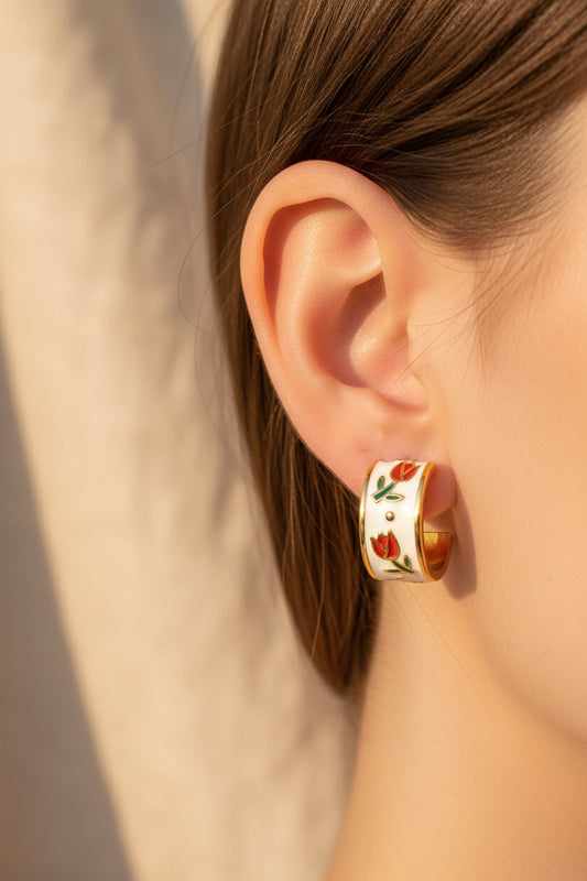 Gold and white earrings with floral design being worn against a beige background