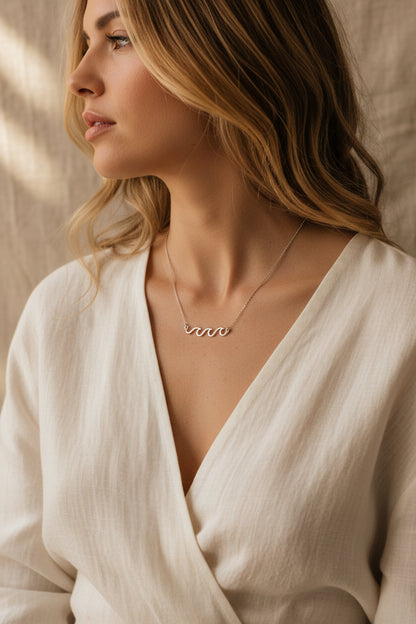 Rhodium dipped necklace with 'Crashing Waves' design and worn here with a natural fiber dress and beige background