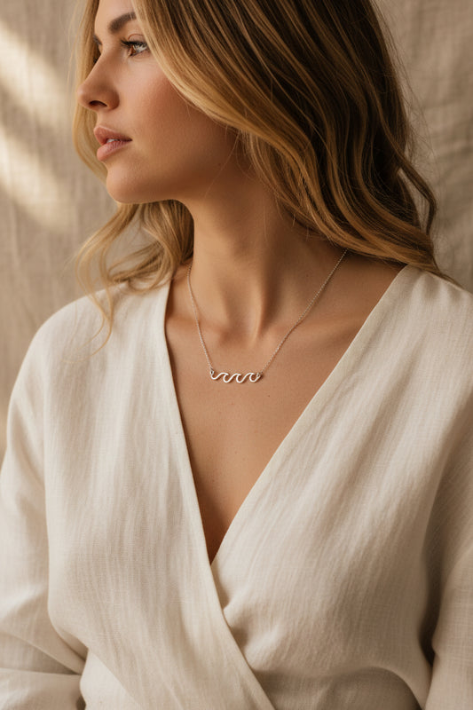 Rhodium dipped necklace with 'Crashing Waves' design and worn here with a natural fiber dress and beige background