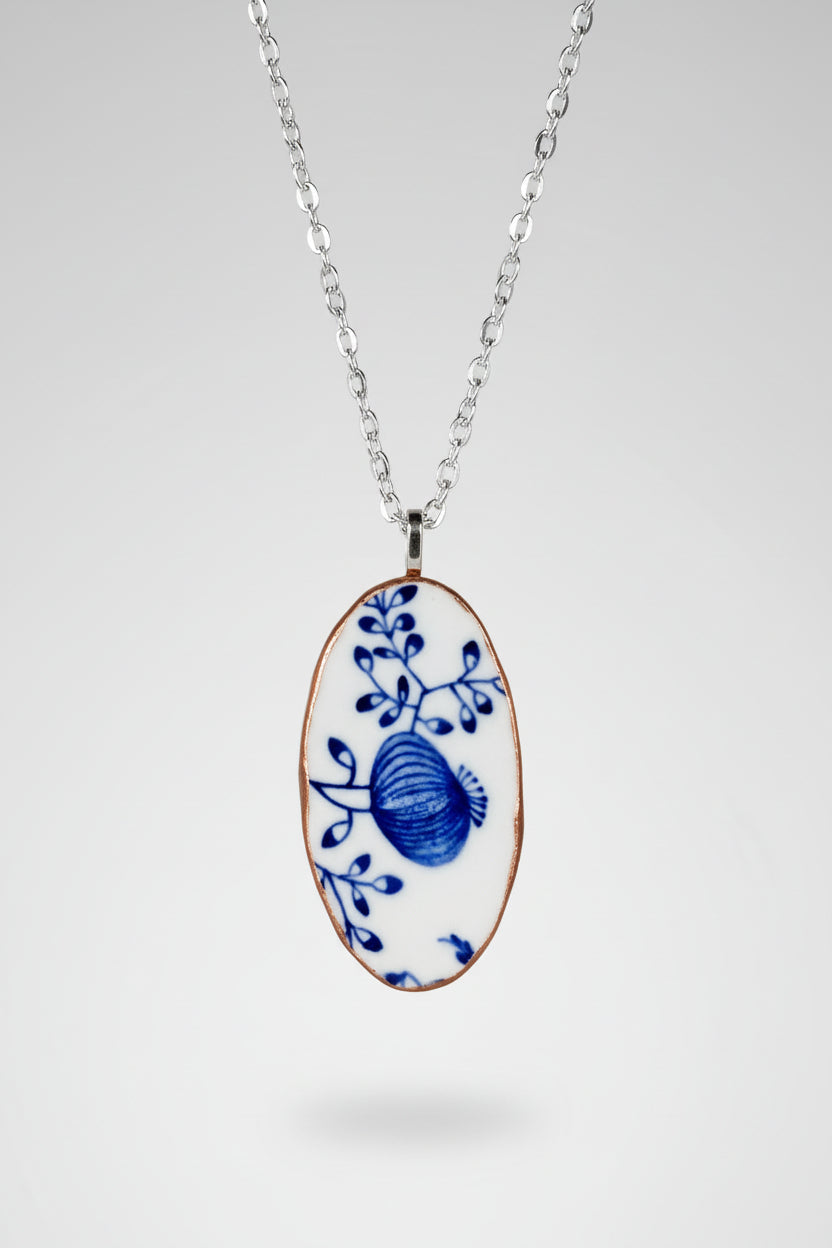 Necklace with an oval pendant featuring white and blue floral design on a plain background