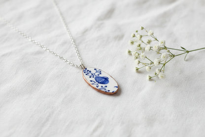 Necklace with an oval pendant featuring blue floral design on a beige background