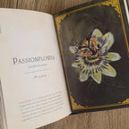 Open book with a passionflower illustration on a wooden surface