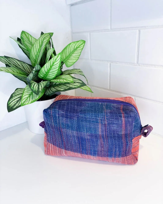 Blue and red checkered pouch on a white surface with a plant in the background