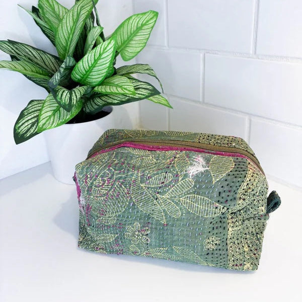 Green patterned toiletry bag on a white surface with a plant in the background