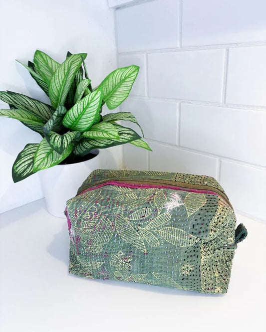 Green patterned toiletry bag on a white surface with a plant in the background