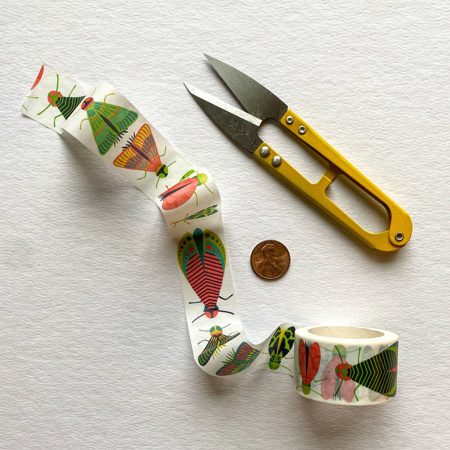 Mondo Bug tape next to scissors and a penny (eluding to size of the tape) with a neutral background