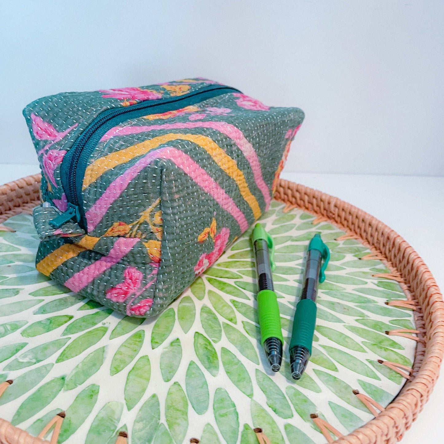 Colorful fabric zippered box pouch with floral patterns on a woven tray with green leaf pattern