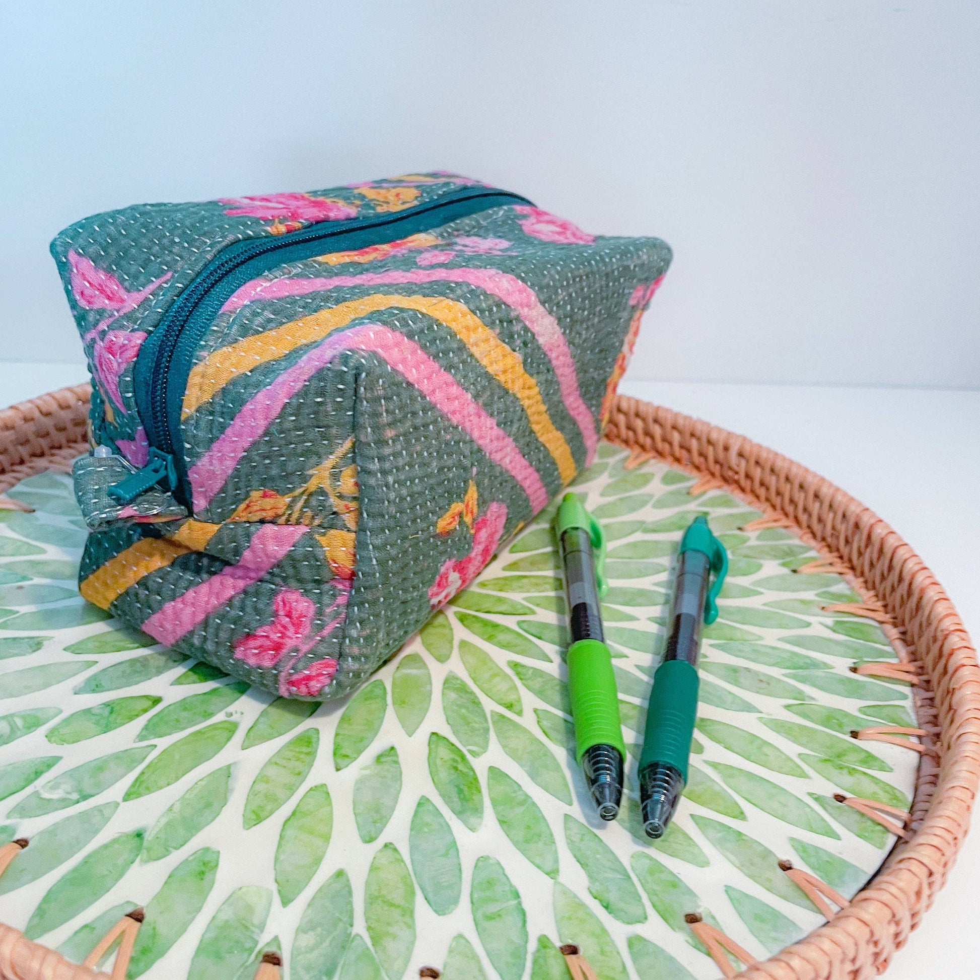 Colorful fabric zippered box pouch with floral patterns on a woven tray with green leaf pattern