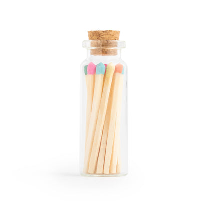 Birthday cake scented candle in white tin with corked vial of colorful matchsticks, packaged in a clear vinyl gift box.