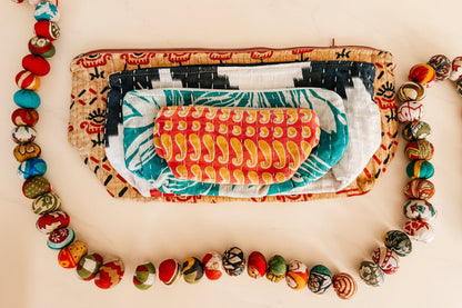 Stack of colorful pouches with patterned contents on a white background and sari garland
