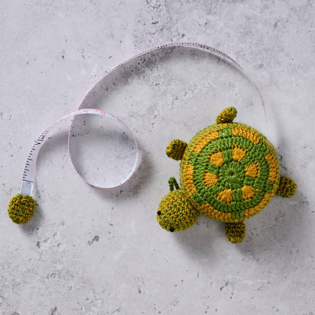 Crocheted turtle toy next to a measuring tape on a concrete surface