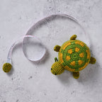 Crocheted turtle toy next to a measuring tape on a concrete surface