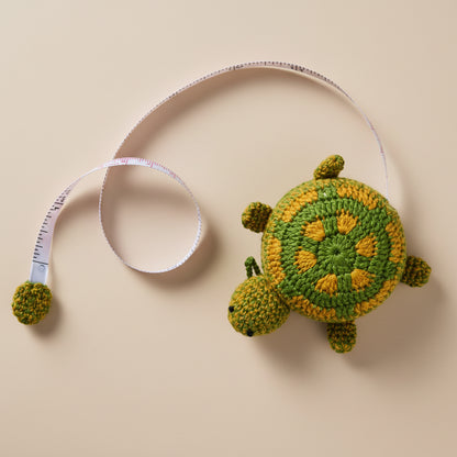 Crocheted turtle toy next to a measuring tape on a concrete surface