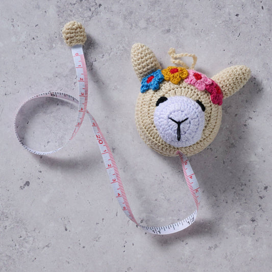 Crocheted llama measuring tape with the measuring tape pulled out on a concrete surface