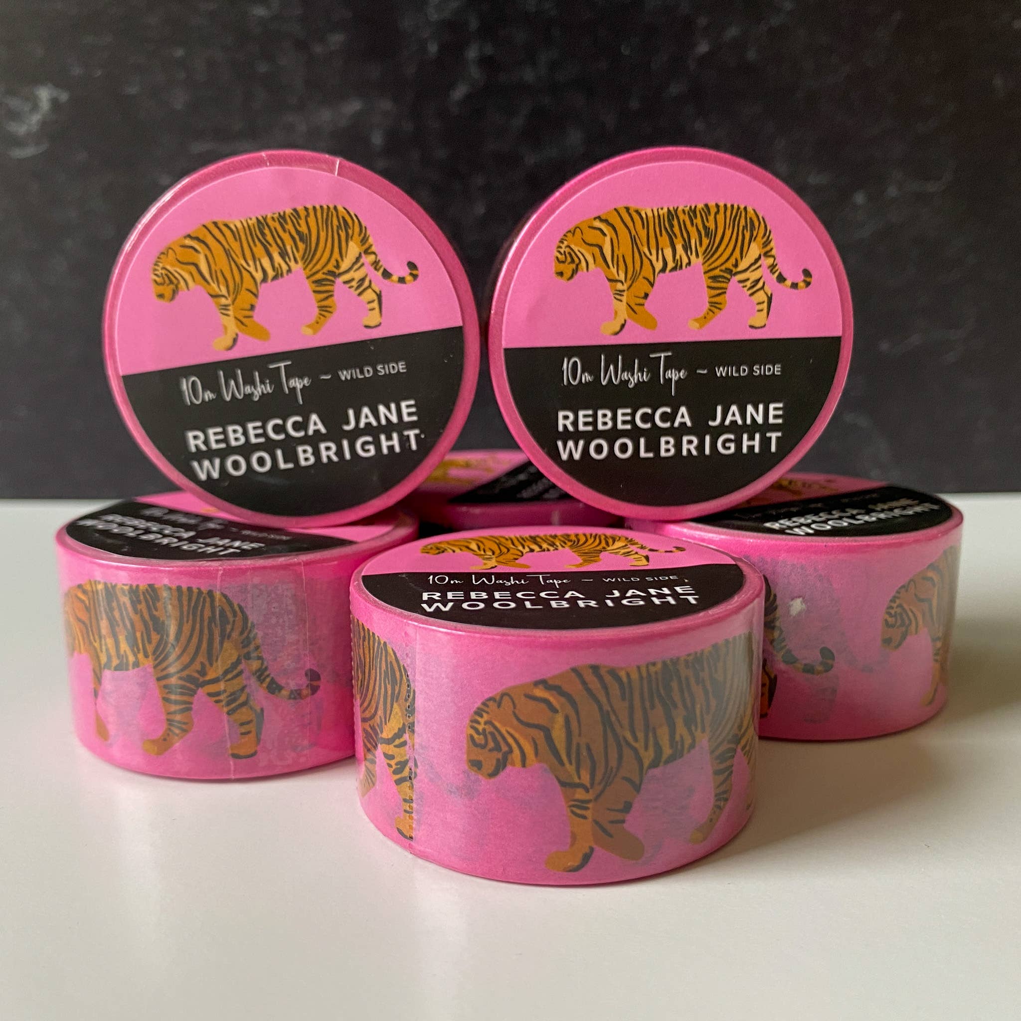 Stack of multiple rolls of the Wild Side washi tape showcasing a bright pink background with handdrawn tiger